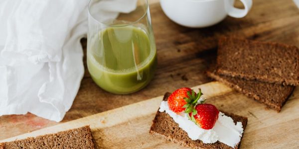 Start your day with a nutritious breakfast featuring rye toast with cream cheese and strawberries, paired with green juice and coffee.