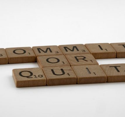 Scrabble tiles spelling 'Commit Or Quit' on a white surface, symbolizing decision-making.