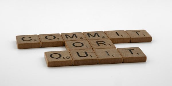 Scrabble tiles spelling 'Commit Or Quit' on a white surface, symbolizing decision-making.
